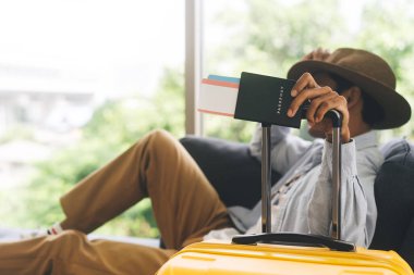 Seyahat eden Asyalı adamın elinde bavul tutacağı pasaport ve uçak bileti var. İnsanlar tatil gezisi konseptine hazırlanıyor. Evdeki ya da oteldeki kanepede uzanan....