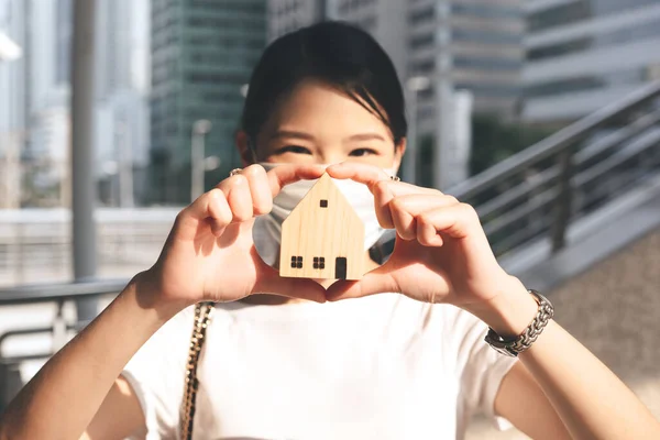 Focus on hand holding house model. Blur young adult business working asian woman background. Residential investment property concept.