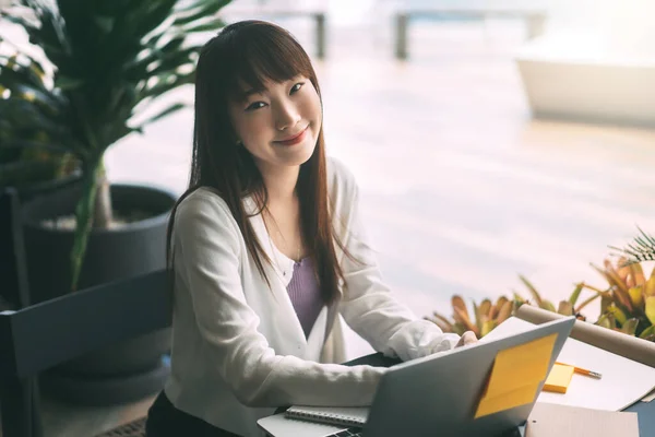 年轻的亚洲大学生女性穿着毛衣的画像 使用笔记本电脑学习 并在咖啡店上网工作 大学生的城市生活方式每天都在外面呆着 — 图库照片