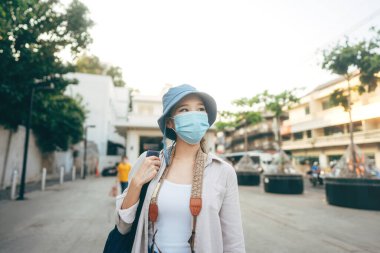 Walking young adult asian woman backpack traveller wear face mask for corona virus or covid-19 and camera. People traveling in city lifestyle at outdoor. Staycation trip concept. Bangkok, Thailand