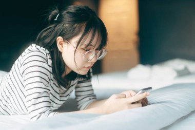 Modern teknoloji konsepti olan bir yaşam tarzı. Genç ve yalnız bir kadın sabahın köründe teletıp ve zihinsel sağlık ve alışveriş için akıllı telefon kullanıyor..