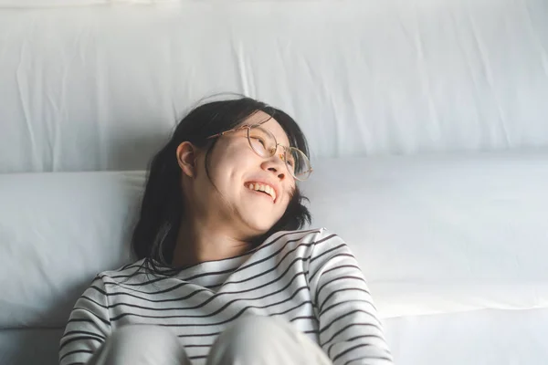 肖像画幸せな若い大人のアジアの女性は 午前中に寝室でリラックス 家にいるか ベッドと枕の上のホテルの残りの部分 居心地の良い場所で眼鏡をよくリラックスしたライフスタイルを着用 — ストック写真