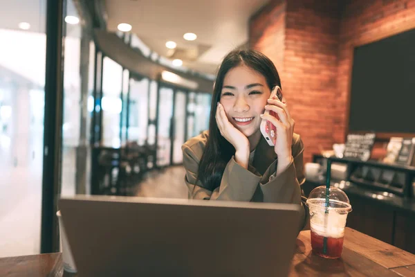 在咖啡店用智能手机打来电话的亚洲年轻的自由职业女性 城市人的生活方式与现代技术日新月异 数字游牧民族 笑容满面 — 图库照片