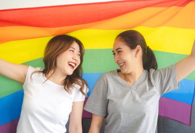 İlişki konseptiyle birlikte yaşayan iki yetişkin kadın. Mutlu gülümseyen güneydoğu Asyalıların portresi gökkuşağı gurur bayrağı taşıyan bir çift. Evdeki hayat anları.