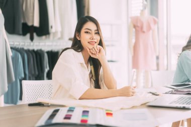 İnsanlar moda tasarım stüdyosu konseptine göre terzi ya da öğrenim görüyor. Genç Asyalı kadın tasarımcı elbise yapmakla meşgul. Bulanık mankenli arkaplan.