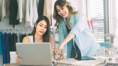Moda tasarımı konseptinde çalışan insanlar. Mutlu bir gülümseme. İki yetişkin Asyalı kadın tasarımcı birlikte konuşuyor. Atölye geçmişi.
