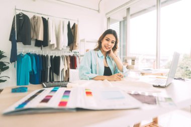 İnsanlar moda giysisi tasarım stüdyosu konseptinde terzilik yapar ya da öğrenim görür. Genç yetişkin Güneydoğu Asyalı kadın tasarımcı dizüstü bilgisayarla meşgul..