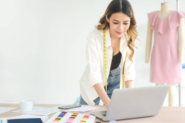 İnsanlar moda giysisi tasarım stüdyosu konseptinde terzilik yapar ya da öğrenim görür. Genç yetişkin Güneydoğu Asyalı kadın tasarımcı dizüstü bilgisayarla meşgul..
