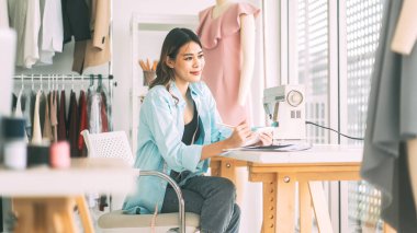 İnsanlar moda tasarım stüdyosu konseptine göre terzi ya da öğrenim görüyor. Genç Asyalı kadın tasarımcı elbise yapmakla meşgul. Dikiş makinesi ve mankenle arka plan.