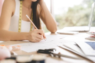 Yakından bakınca, genç ve güzel bir kadın tasarımcının kalemle çizim yapma fikri. Moda donanımlı işyeri masası