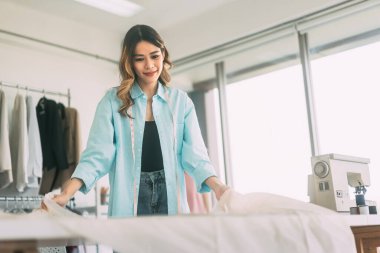 Moda tasarımı sanatını iş başında tecrübe edin. Genç, güneydoğu Asyalı bir kadın tasarımcı atölyede kıyafet tasarımlarını canlandırıyor. Tutkulu ve stili olan girişimci