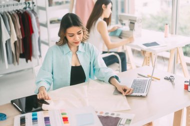 İnsanlar moda tasarım stüdyosu konseptine göre terzi ya da öğrenim görüyor. Genç Asyalı kadın tasarımcı elbise yapmakla meşgul. Dikiş makinesi ve mankenle arka plan.