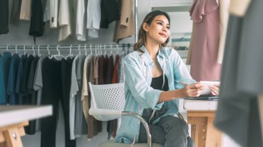 İnsanlar moda tasarım stüdyosu konseptine göre terzi ya da öğrenim görüyor. Genç Asyalı kadın tasarımcı elbise yapmakla meşgul. Dikiş makinesi ve mankenle arka plan.
