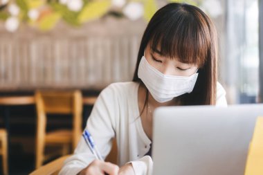 Virüs koronası ya da kovid 19 için koruyucu yüz maskesi olan genç bir Asyalı kadın. Pandemik yaşam tarzı konsepti sırasında Cafe New normal iş ekonomisinde çalış ve çalış. Gün içinde kapalı..