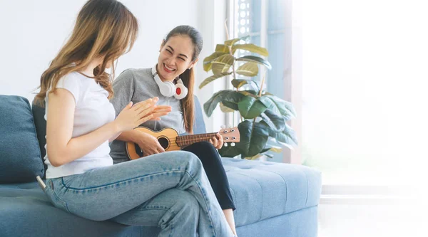 Two young adult woman living together with relationship concept. Southeast asian people couple relax lifestyle playing music on sofa life moments at home. Banner size background.