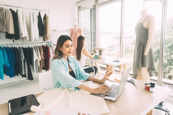 stock image People tailor work or study in fashion cloth design studio concept. Young adult southeast asian woman designer busy using laptop computer.