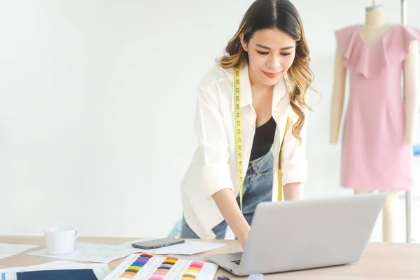 İnsanlar moda giysisi tasarım stüdyosu konseptinde terzilik yapar ya da öğrenim görür. Genç yetişkin Güneydoğu Asyalı kadın tasarımcı dizüstü bilgisayarla meşgul..