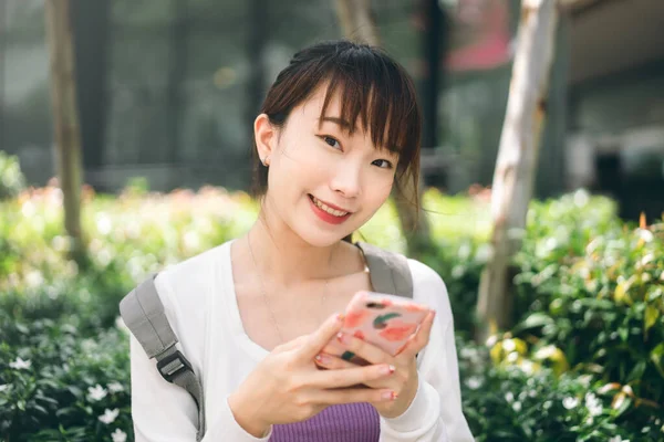 College people lifestyle on day time concept. Young adult asian student woman using mobile phone for online application at outdoor.