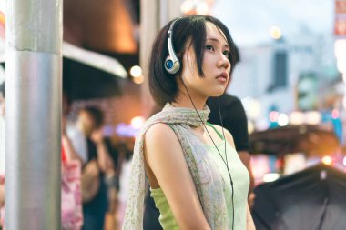 Şehir merkezinde gerçek insan yaşam tarzları. Genç Asyalı bir kadın, kulaklıkla 2k nostalji modası kıyafeti giyer. Asya Çin Mahallesi Yemek Gecesi Marketi Bangkok, Tayland