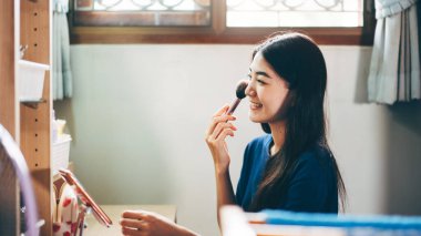 Bekar olmak, sağlıklı ve mutlu bir yaşam tarzını gündüz konseptine hazırlar. Genç Asyalı kadın makyajı ve yüz derisi aynanın önünde evdeki elbise odasında..