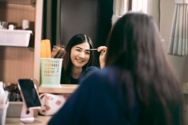 Portrait of single stills wellness lifestyle ready for day concept. Young adult asian woman makeup and face skincare before mirror in dress room at home. 