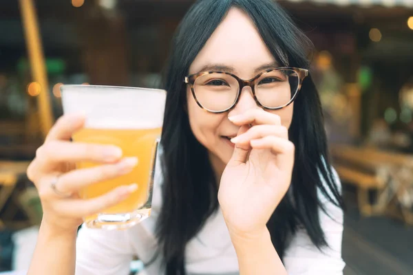 Portrait of young adult asian woman with eyeglasses drinking beer at restaurant outdoor area. People relax in city break concept.