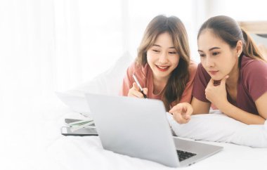 Samimi lezbiyen bir çiftin aşkı ve birlikteliği. Birlikte yaşayan Asyalı kadınlar, beyaz bir yatakta uzanıyorlar, dinlenmek için dizüstü bilgisayar kullanıyorlar. Modern bir yaşam tarzında huzurlu ve neşeli anlar.