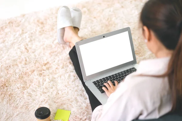 Blank white screen laptop for copy space with woman hand typing keyboard from back shoulder view. People sitting on carpet background.