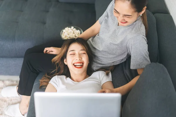 Two young adult woman living together with relationship concept. Southeast asian people couple relax lifestyle on sofa eating popcorn life moments at home or apartment.