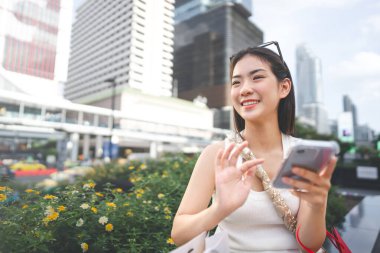 İnsanlar şehir yaşam tarzlarını alışveriş tüketimiyle satın alıyorlar. Genç, Asyalı bir kadın akıllı telefon yazma mesajı kullanıyor. Dijital cüzdan bankası ödemesi. Mutlu yüz dışarıda oturuyor..