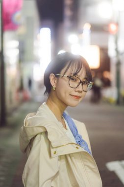 Gece hayatı Asyalıların portresi. Japon Tokyo şehri yalnız, gözlüklü genç yetişkin kadın. Bokeh neon ışıklı şehir arkaplanı.