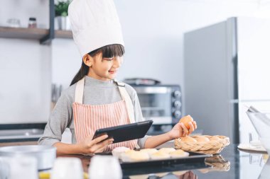 Aşçı şapkası ve önlüğüyle mutfakta yemek pişiren küçük Asyalı kız. Ev yapımı yemekler ve boş yaşam tarzları. Faiz becerisi olan çocuk büyümesi.