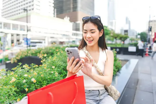 People city lifestyles with buying shopping consumerism. Young adult asian woman using smartphone typing message social media. Happy smile face sitting at department store.