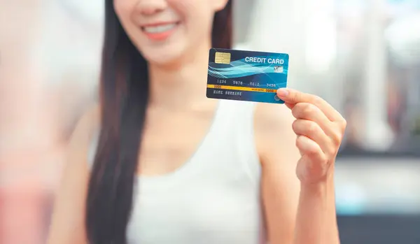 İnsanlar şehir yaşam tarzlarını tüketicilikle satın alıyorlar. Kapalı kapılar ardında alışveriş ve seyahat için kredi kartı tutan bir kadın. Nakitsiz alışverişe para harcamak. Kopyalama alanı ile gülen yüz arkaplanı.