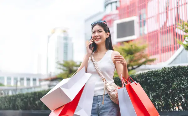 People city lifestyles with buying shopping consumerism. Young adult asian woman using smartphone for digital wallet banking. Happy smile face standing at outdoor.