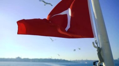 Mavi gökyüzü arka planında Türk Bayrağı dalgalanıyor, rüzgarda sallanıyor.