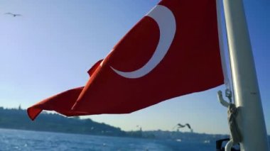 Mavi gökyüzü arka planında Türk Bayrağı dalgalanıyor, rüzgarda sallanıyor.