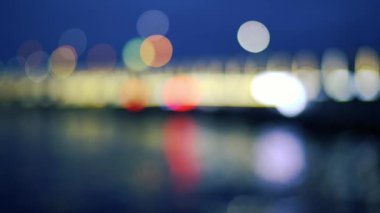 Gecenin karanlığında parlak ışıkların yönünü değiştiriyorum. Bokeh ışığı etkisi. Köprü ve deniz ışıkları.