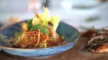 Parmesanlı rendelenmiş taze tavuk salatasının üzerine yavaş çekimde marul ve cips dökülüyor..