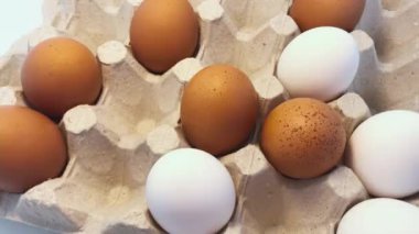 White and brown raw chicken eggs in a grey egg container.