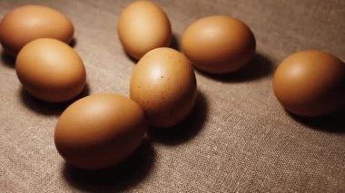 Seven brown raw chicken eggs on a brown linen bedspread.
