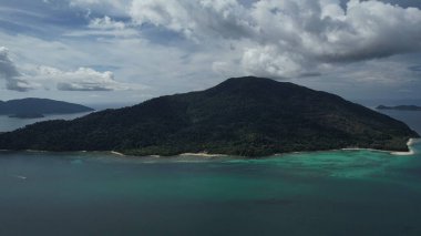 Etrafı dağlarla, ağaçlarla ve gölle çevrili küçük bir adanın havadan görünüşü. Gökyüzü kümülüs bulutlarıyla dolu ve ufuk büyüleyici.