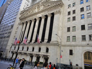 Bir grup yaya ikonik New York Borsa binasının önünden geçerken şehrin hareketli metropolündeki büyük cephesine hayran kalıyorlar.