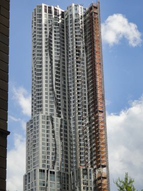 New York 'ta birkaç ağaç ve eve yayılmış kentsel tasarım binalarıyla çevrili, açık mavi gökyüzüne karşı dimdik duran modern bir gökdelen.