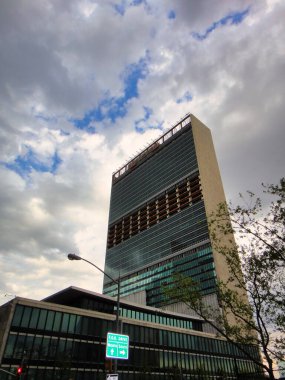 New York şehrinde yükselen bir gökdelen cephede Birleşmiş Milletler işareti olan kümülüs bulutları arasında uzanıyor.