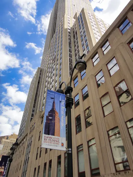 Bulutlu gökyüzüne karşı Empire State Binası tabelasıyla yükselen gökdelende, New York 'ta gündüz vakti şehir tasarımı sergileniyor.