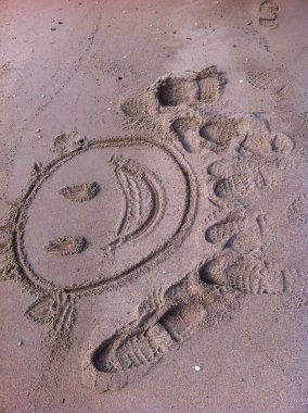 Kumsalda kumlara gülen bir yüz çizilir.