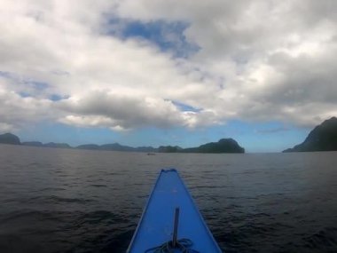 Mavi bir su aracı sakin bir göl boyunca seyahat eder, sakin sularda yansıyan gökyüzü, resmedilmeye değer doğal bir manzara olan Palawan Filipinleri 'ni yaratır.