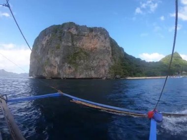 Palawan Filipinleri 'nde bulutları kabarık, berrak bir gökyüzünün altında, arka planda görkemli bir dağla huzurlu bir göl gezen bir tekne.
