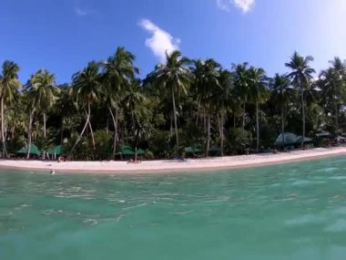 Palmiye ağaçlarının kumlu bir sahili kapladığı doğal bir manzara ve sakin bir su kütlesi. Temiz sıvı gökyüzünü ve beyaz bulutları yansıtıyor Palawan Filipinleri üzerinde